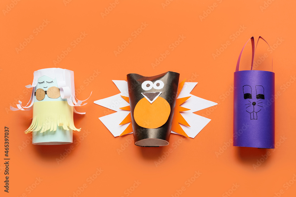 Doll, bird and rabbit made of cardboard tubes for toilet paper on orange background