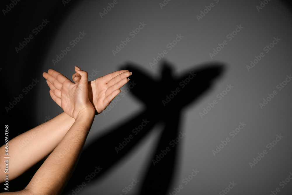 Woman making shadow bird with her hands on dark background