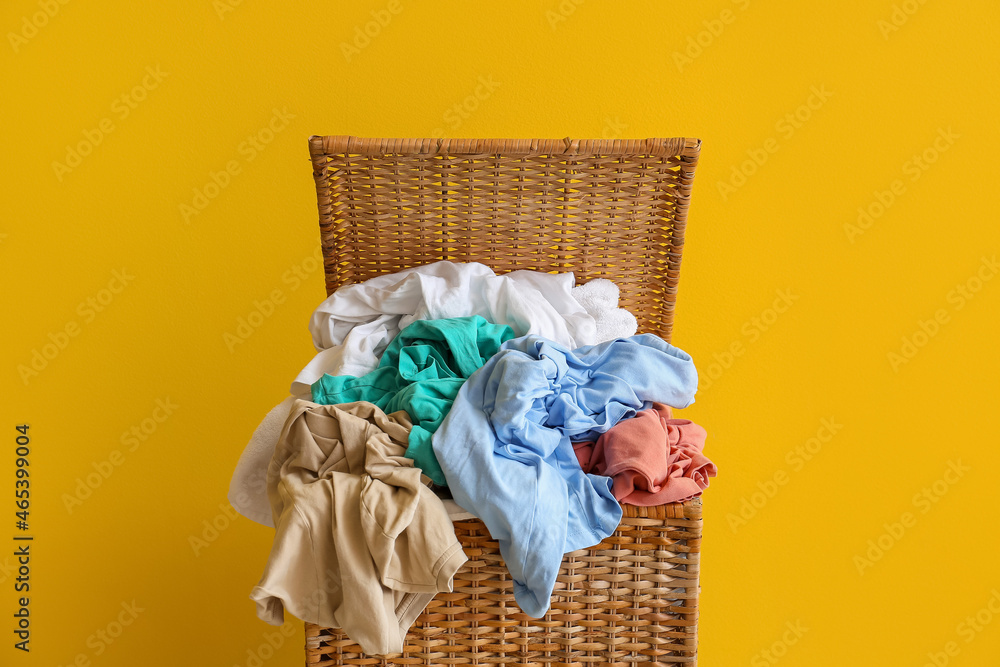 Wicker basket with dirty clothes on yellow background