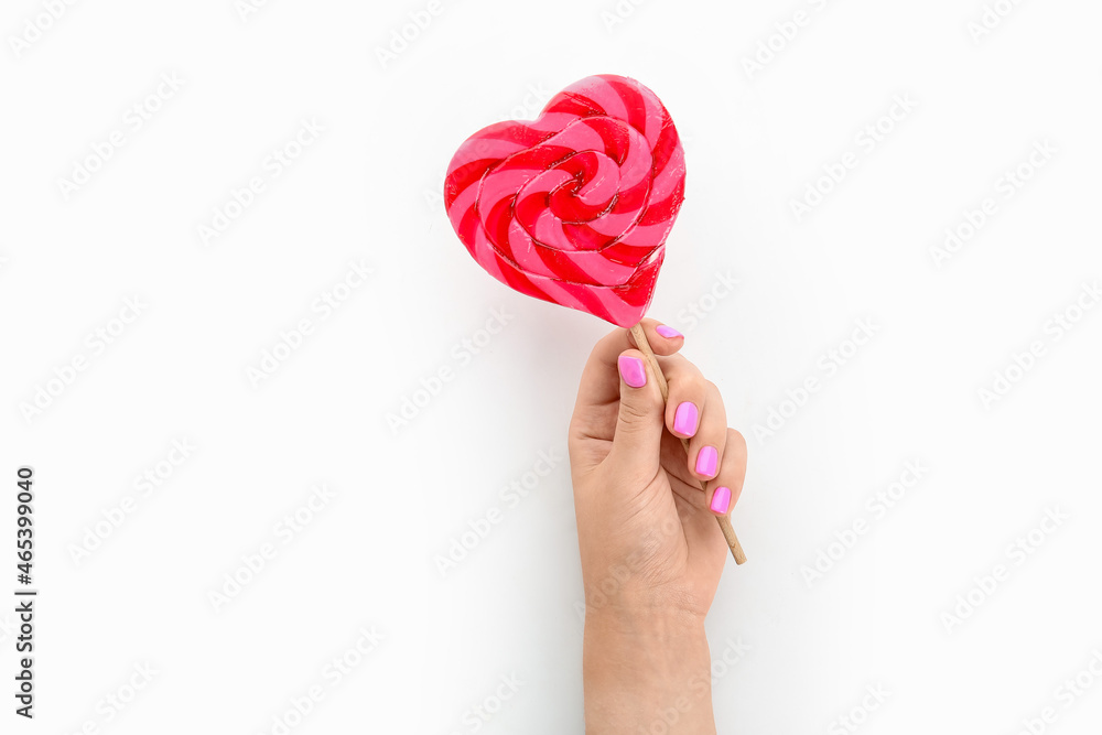 Woman with beautiful manicure holding heart shaped lollipop on white background