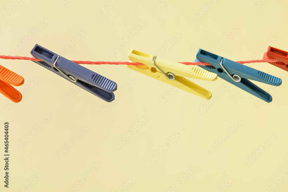 Different clothespins hanging on laundry line against color background, closeup