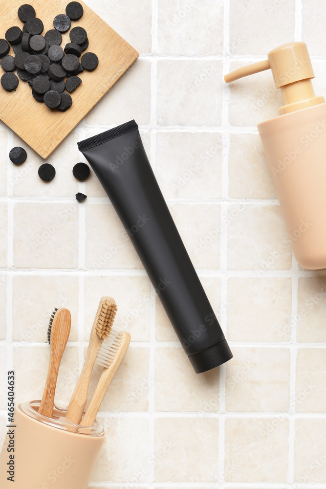 Black toothpaste with activated carbon, pills, brushes and soap on bath tile background