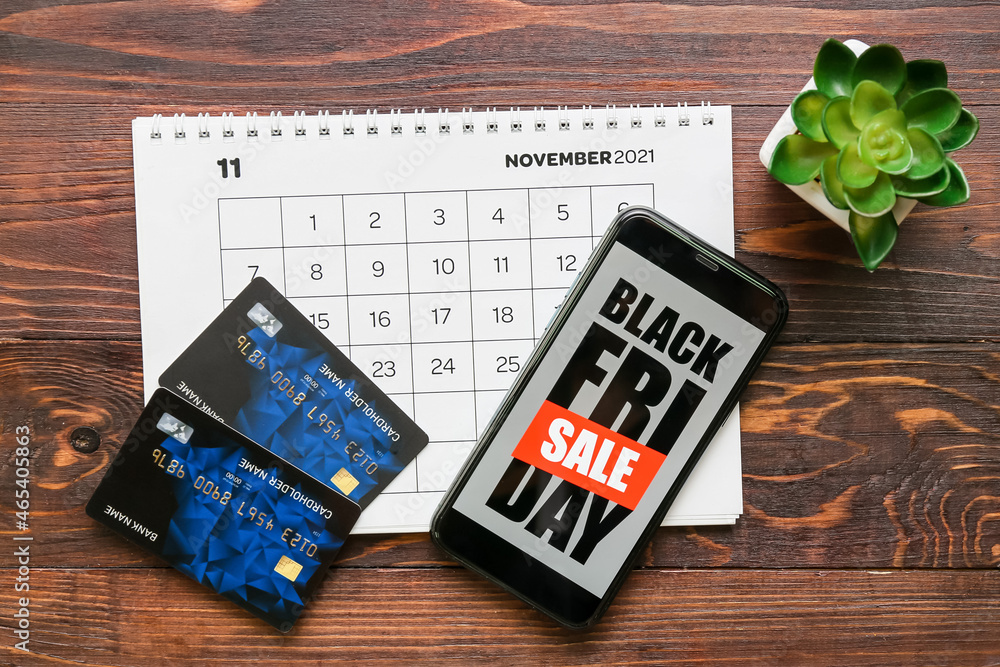 Mobile phone with text BLACK FRIDAY SALE, calendar and credit cards on dark wooden background