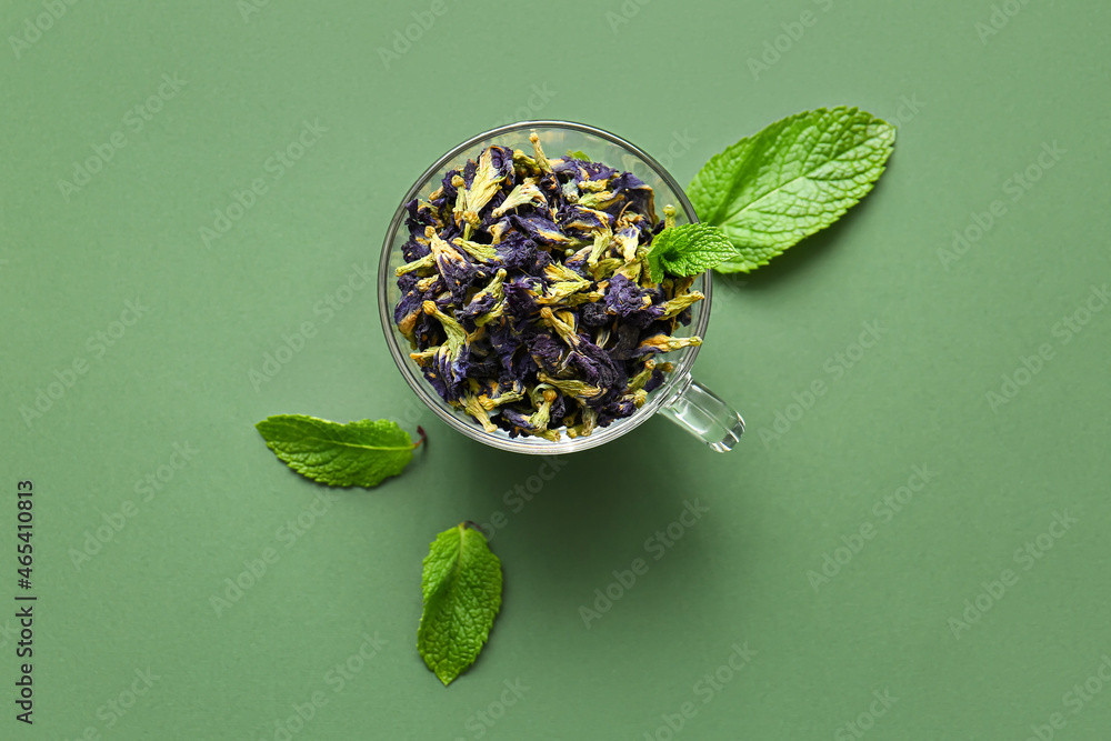 Glass cup of dried butterfly pea flower tea on color background