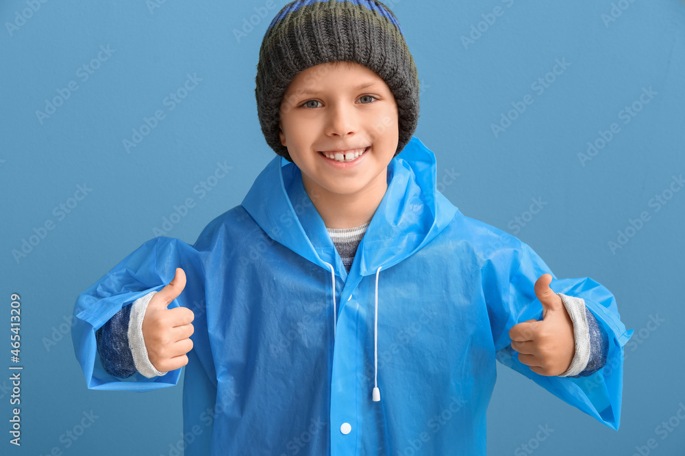 Little boy in raincoat showing thumb-up on color background