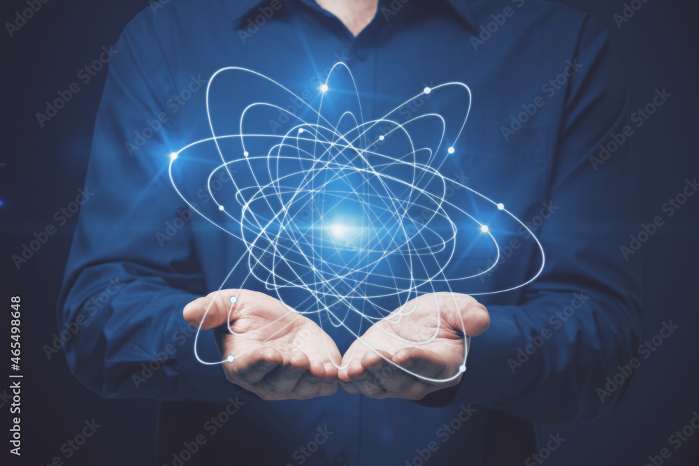 Businessman holding atom on dark background. Science concept.