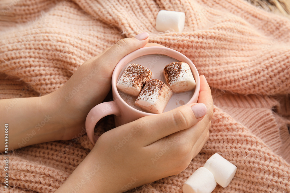 Female hands with cup of cacao and sweater on table, closeup