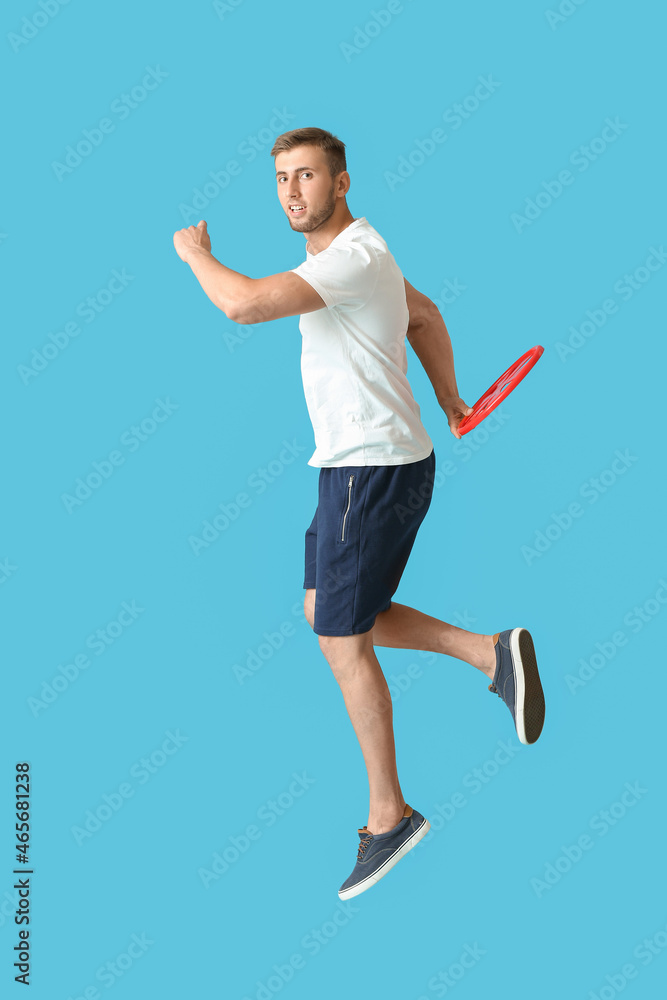 Handsome young man playing frisbee on blue background