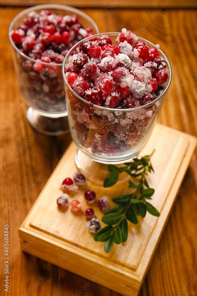 Glass bowls with tasty sugared cranberries on wooden background