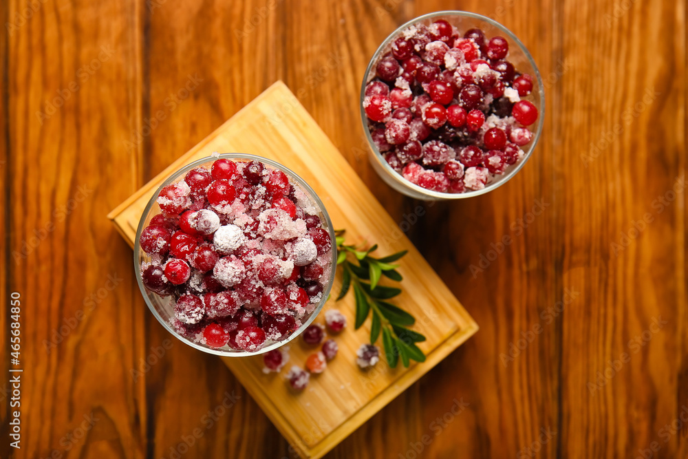 Glass bowls with tasty sugared cranberries on wooden background