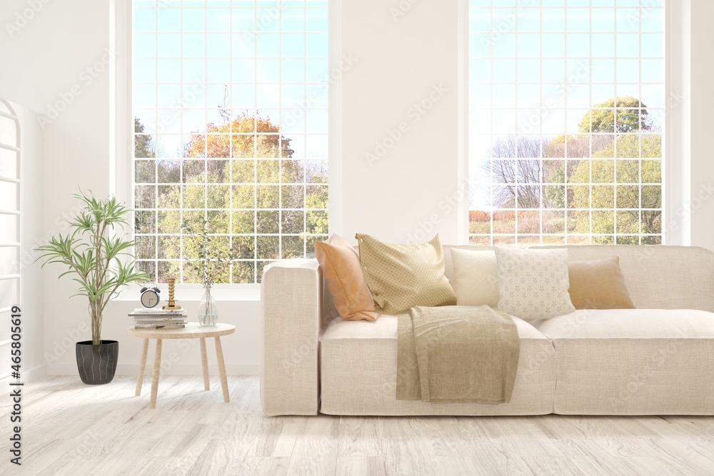 Stylish room in white color with sofa and autumn landscape in window. Scandinavian interior design. 