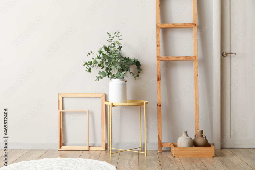 Vase with green eucalyptus branches on table near light wall