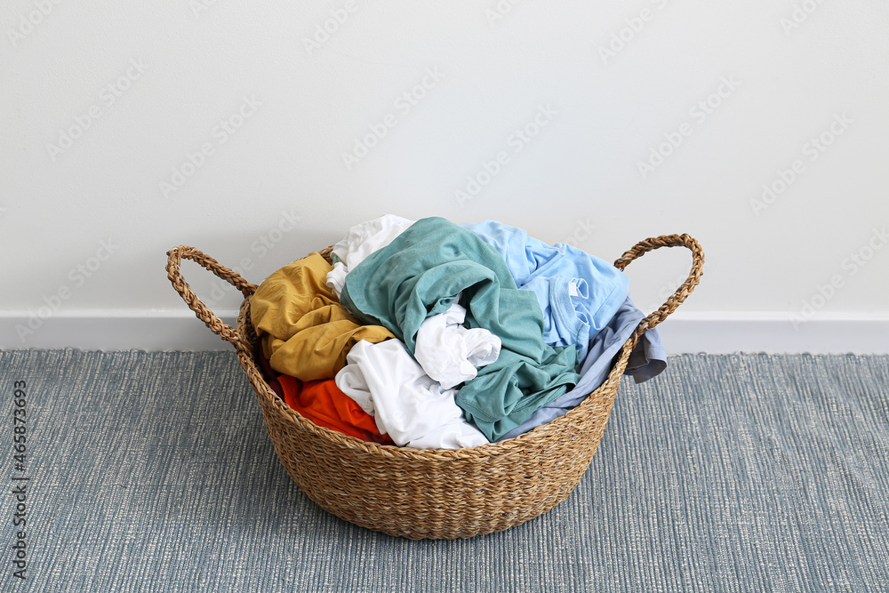 Wicker basket with laundry on blue rug near light wall