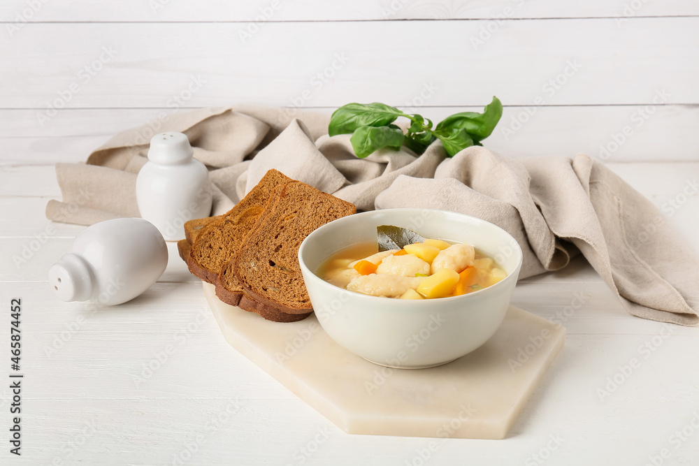 Bowl with delicious dumpling soup and bread on light wooden background