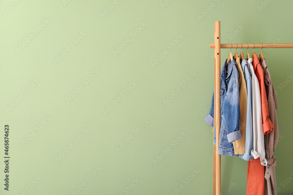 Rack with stylish jackets near green wall