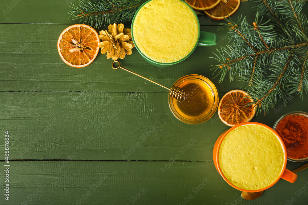 Cups of tasty turmeric latte with honey and fir branches on color wooden background