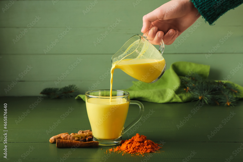 Woman pouring healthy turmeric latte from jug into cup on table