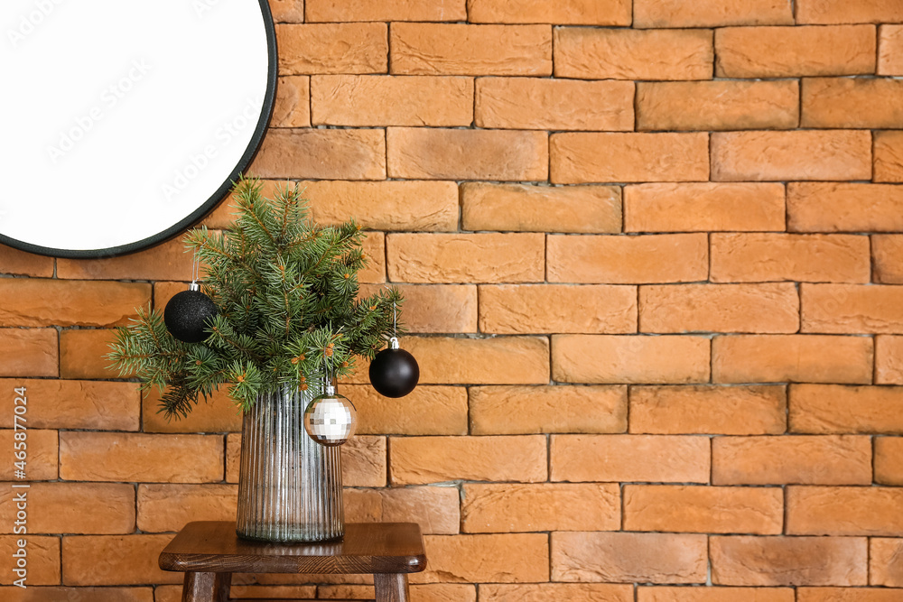 Vase with fir branches and Christmas balls on table near brick wall