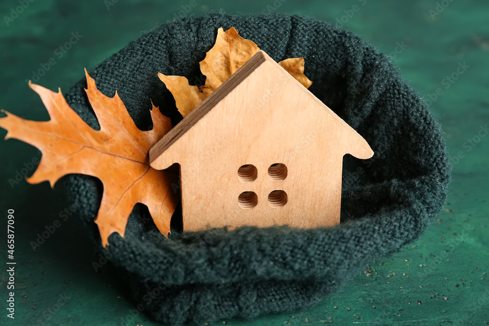 House figure with fallen leaves and warm hat on green background