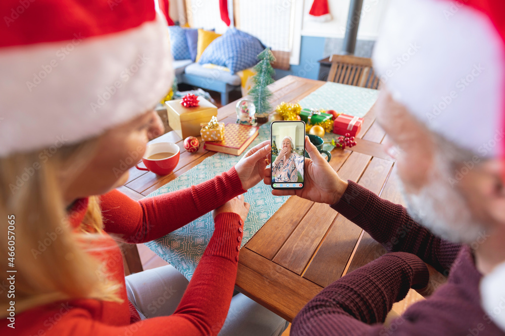 Caucasian couple in santa hats making christmas smartphone video call with happy senior woman