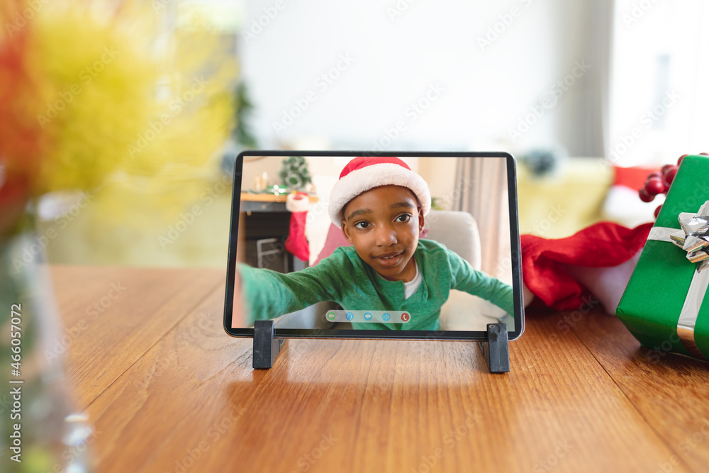 Happy african american boy in christmas santa hat smiling on smartphone video call interface screen