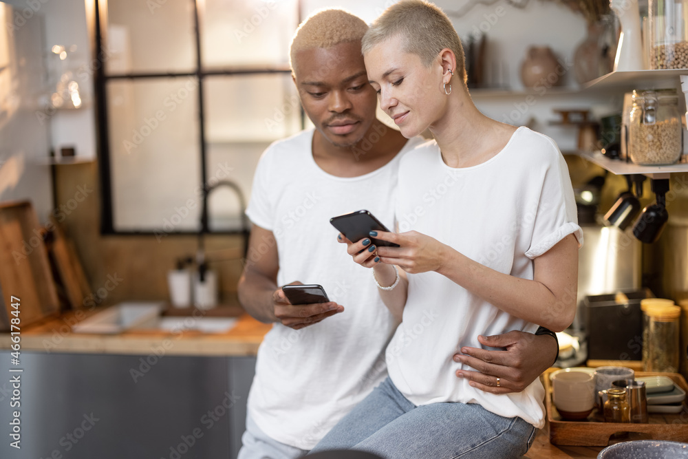 Multiracial couple using mobile phone together at home kitchen. Concept of relationship. Idea of mod