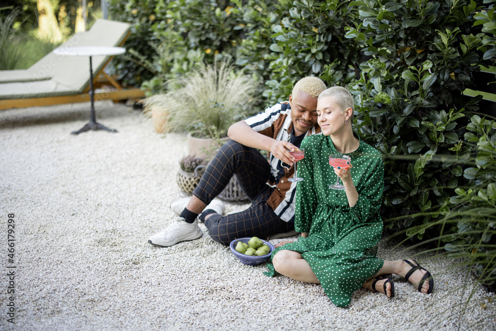 Multiracial couple drinking cocktails at home garden. European girl and black man spending time toge