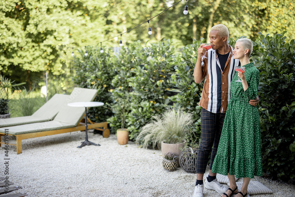 Multiracial couple drinking cocktails at home garden. European girl and black man spending time toge