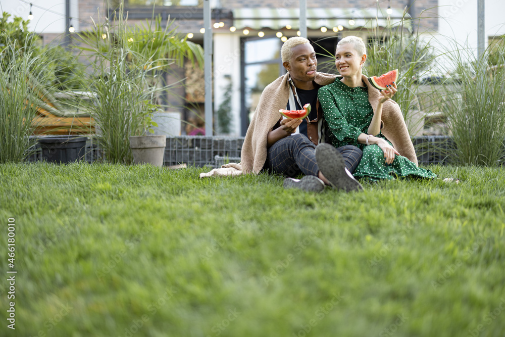 Multiracial couple eating watermelon in their garden. Concept of relationship and enjoying time toge