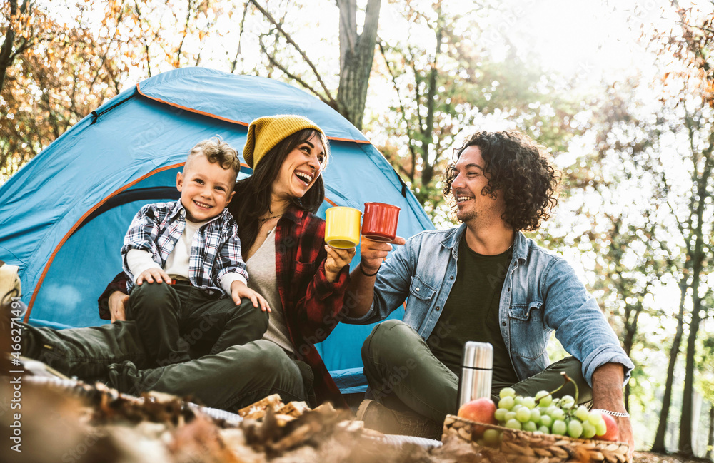 Happy family camping in the forest drinking tea sitting in touristic tent - Mother, father and son h