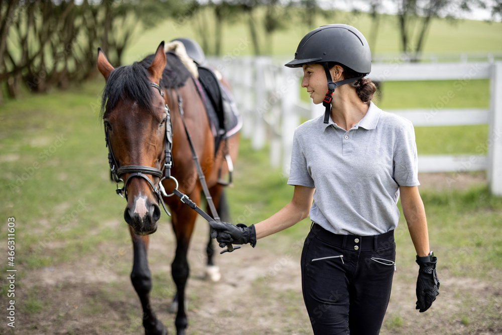 Female horseman going on meadow with her brown Thoroughbred horse. Concept of animal care. Rural res