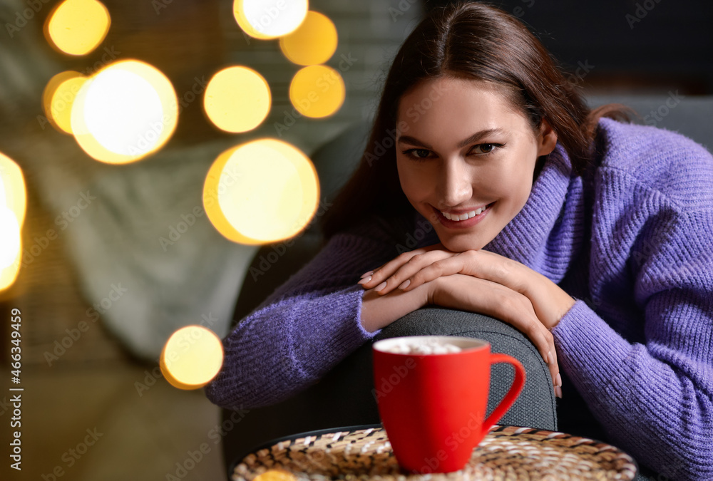 Beautiful young woman with cup of hot cacao drink at home on Christmas eve