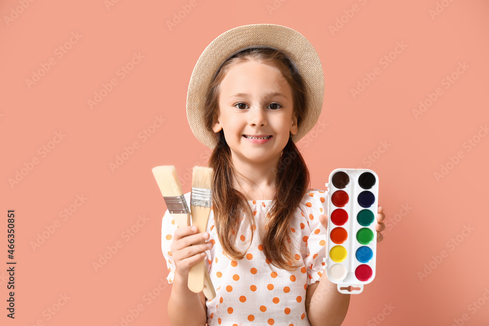 Cute little girl with brushes and watercolor paints on pink background