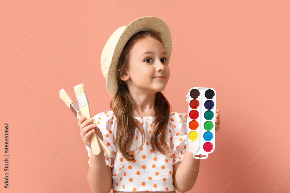 Cute little girl with brushes and watercolor paints on pink background