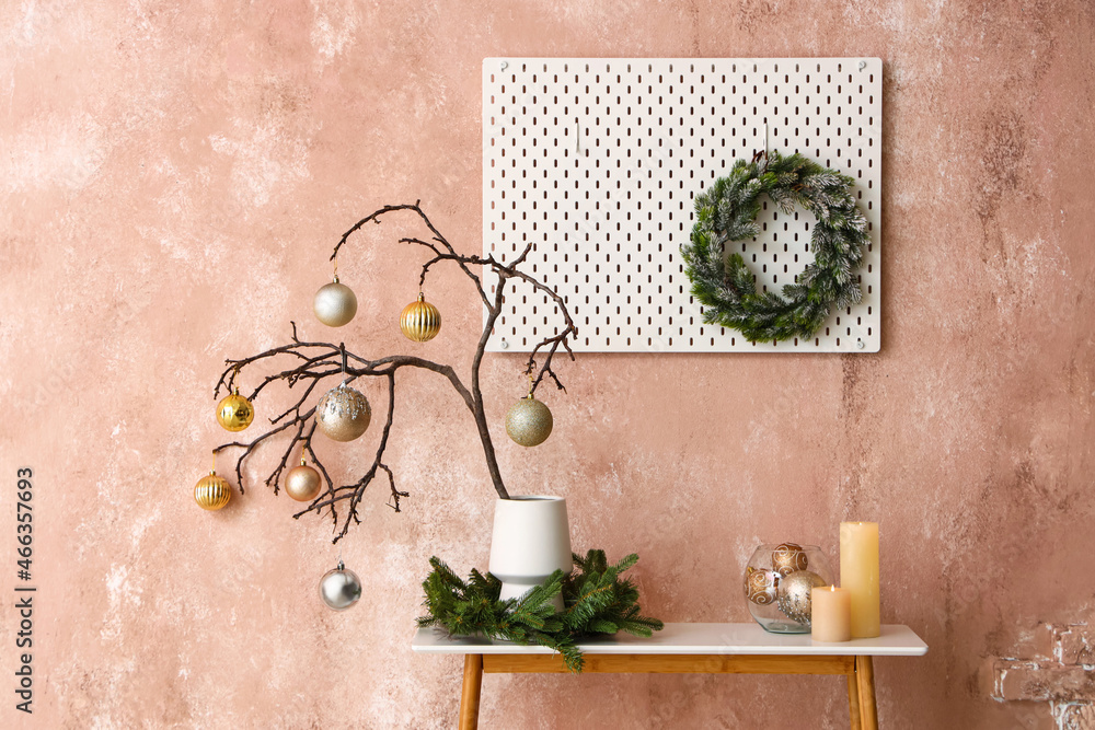 Tree branches with Christmas balls in vase and candles on table near pink wall