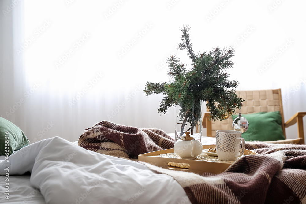 Vase with fir branches, teapot and cup on tray in bedroom