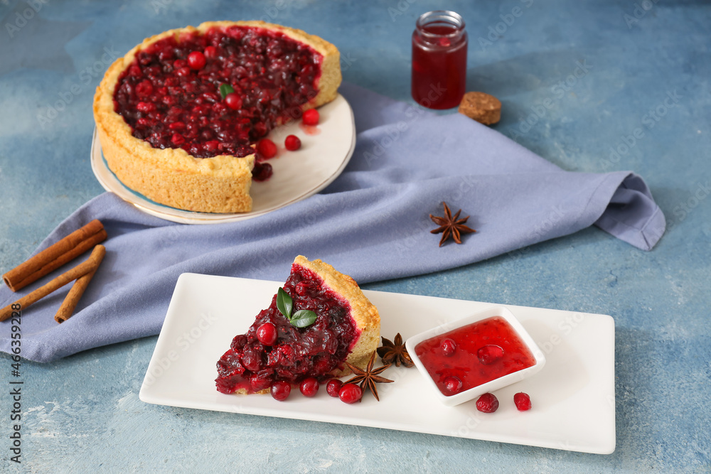 Plate with piece of tasty lingonberry pie, spices and jam on color background