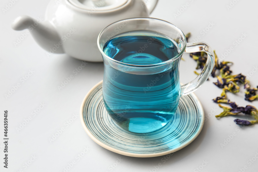 Glass cup of organic blue tea and dried flowers on white background, closeup