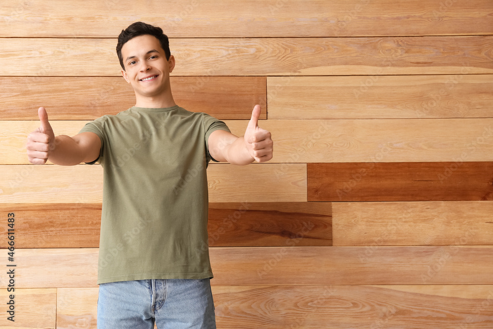 Handsome young man in stylish t-shirt showing thumb-up on wooden background