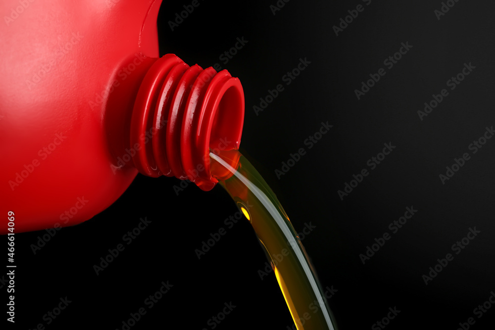 Pouring of motor oil from canister against black background, closeup