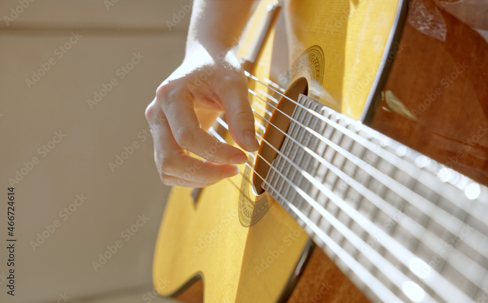 Closeup of a boy playing guitar indoors with sun shining on the guitar