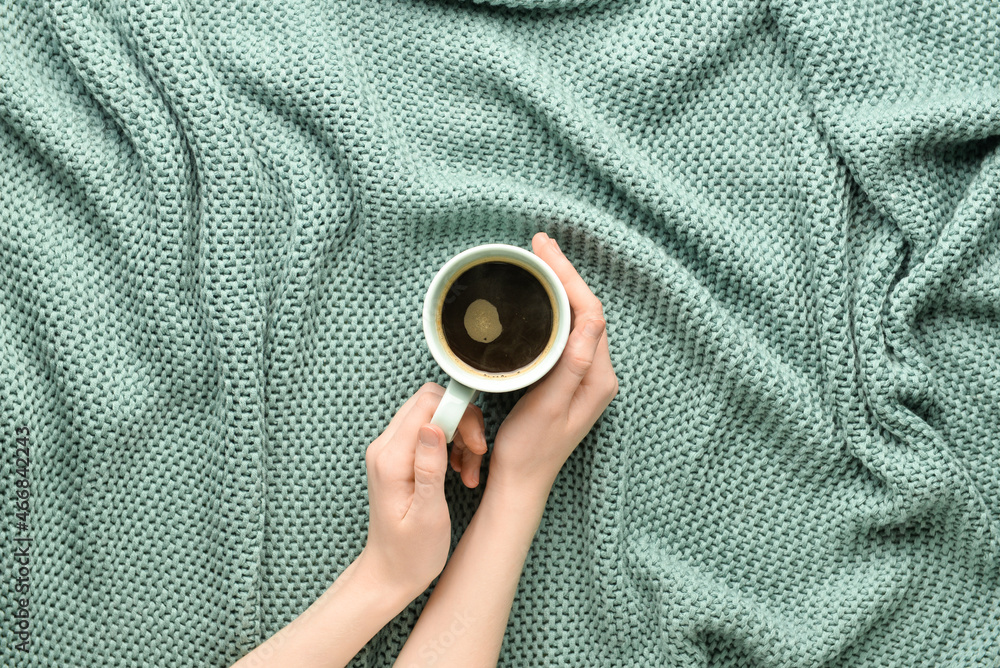 Woman holding cup of coffee on color fabric background