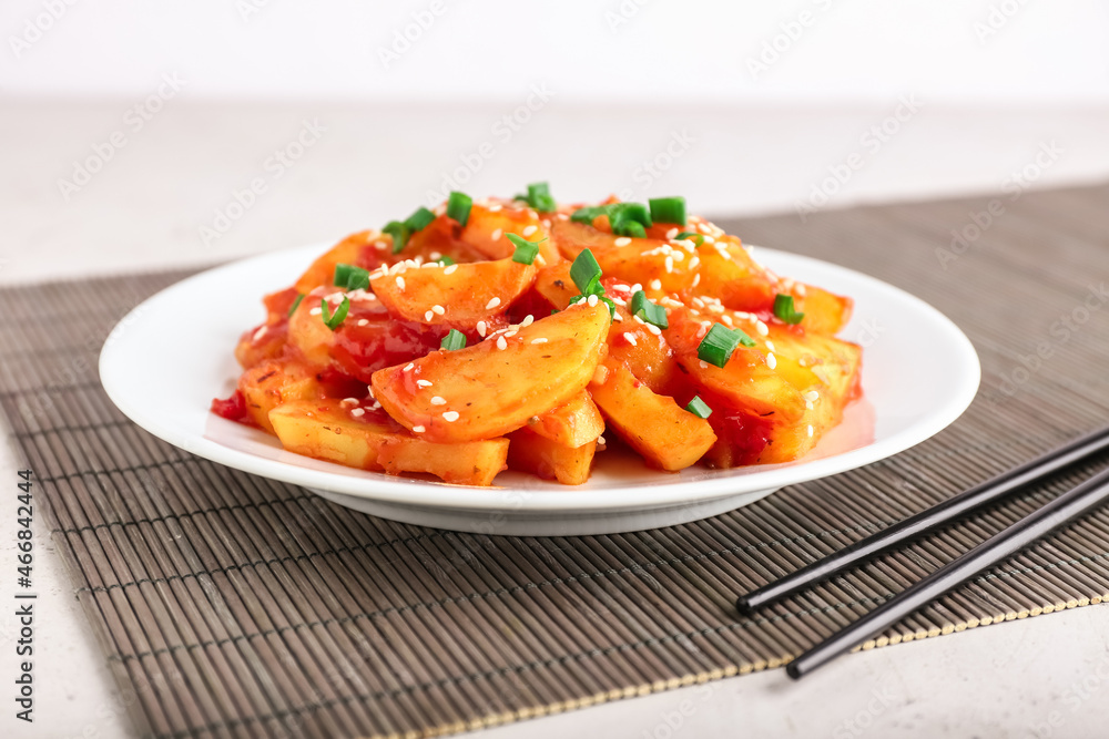 Plate with honey chilli potato and chopsticks on table