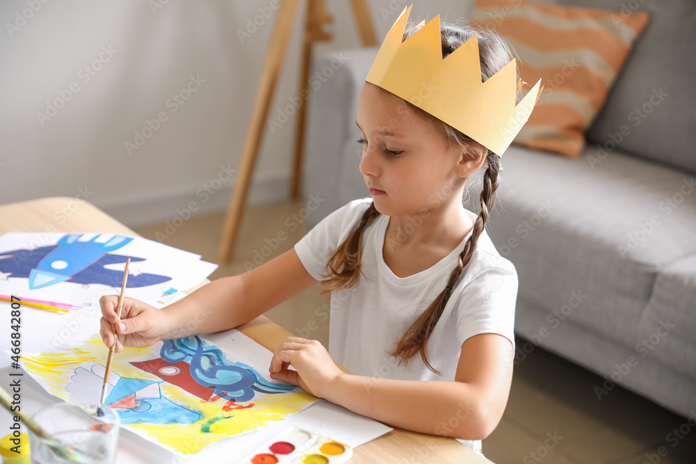 Little girl in paper crown painting with watercolors at home