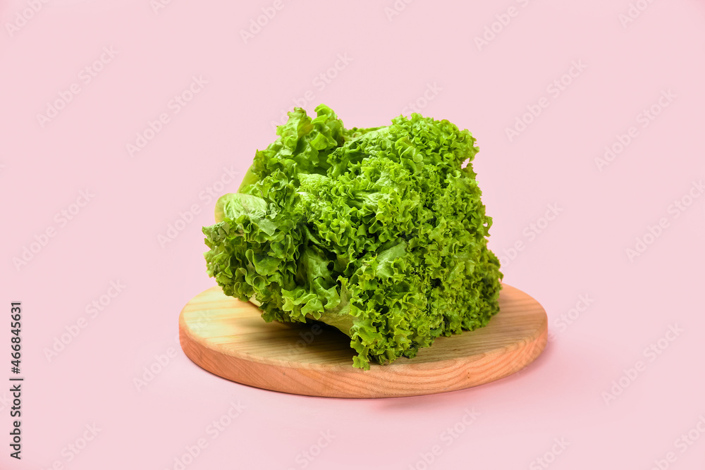 Wooden board with fresh lettuce on pink background