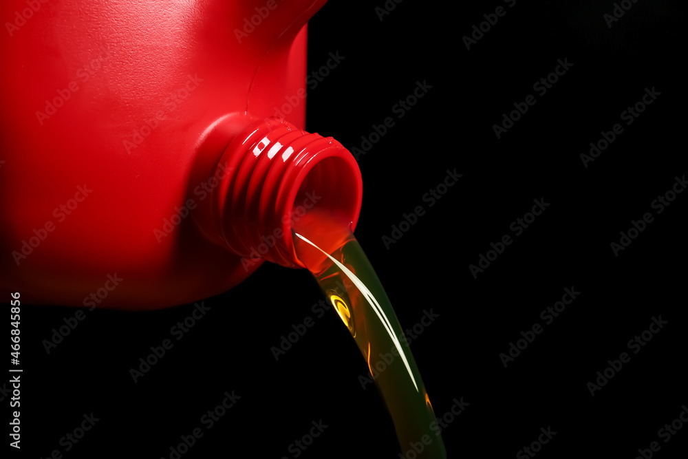 Pouring of motor oil from canister against black background, closeup