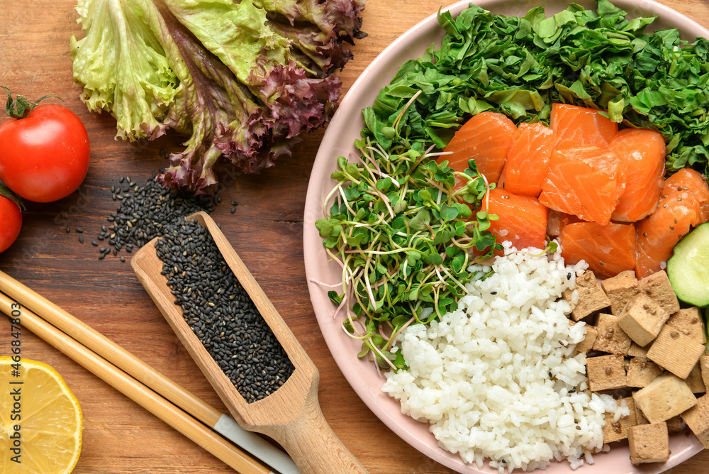 Plate with tasty rice, salmon, tofu cheese and vegetables on wooden background