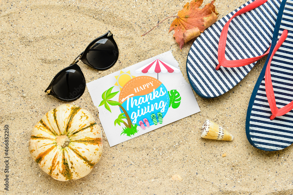 Pumpkin, sunglasses, flip flops, dry leaf, seashell and paper card with text HAPPY THANKSGIVING on s