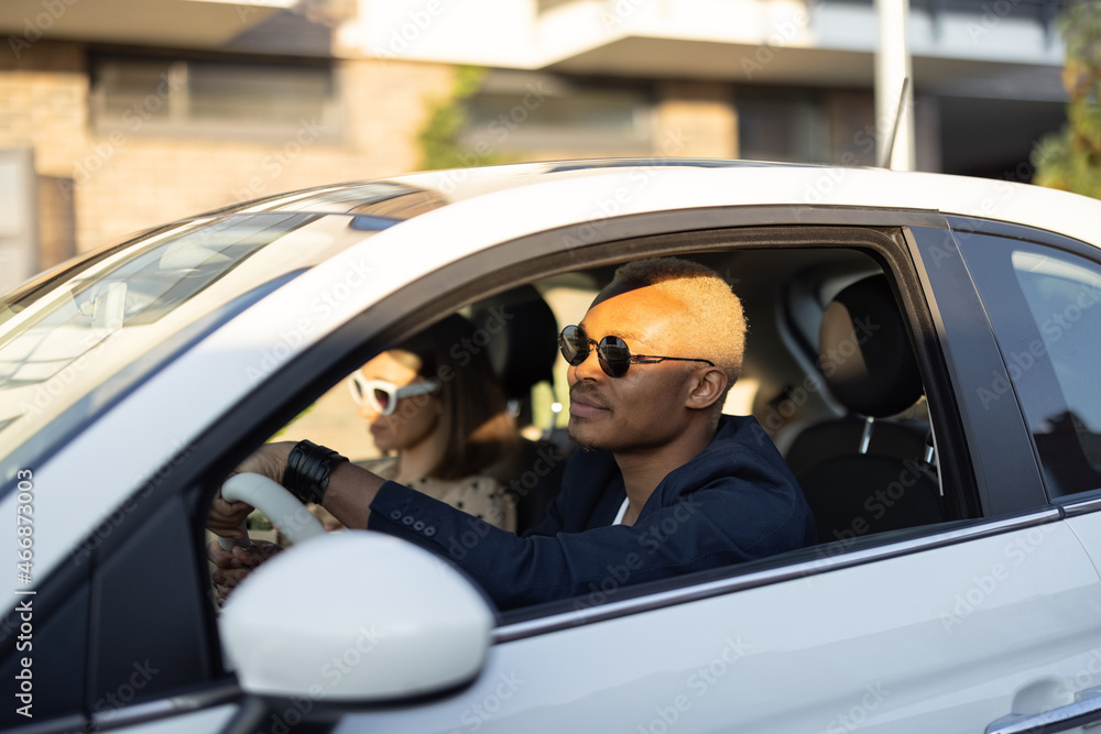 Young happy multiracial couple driving at car together. Latin businessman on the drivers seat with h