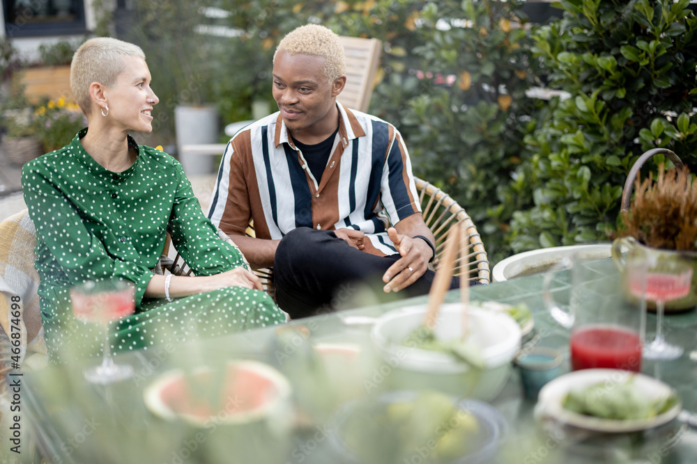 Multiracial couple talking and having fun during a dinnertime at their garden of country house. Idea